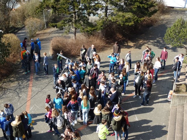 Schülerinnen und Schüler beobachten die Sonnenfinsternis auf dem Schulhof